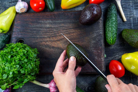 Closeup image of a woman cutting and chopping avocado by knife on wooden boardの写真素材