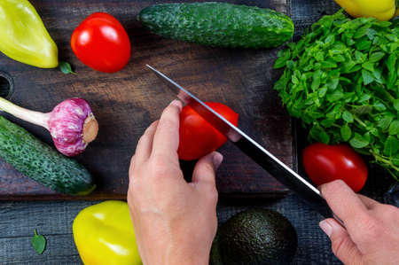 Closeup image of a woman cutting and chopping tomato by knife on wooden boardの写真素材