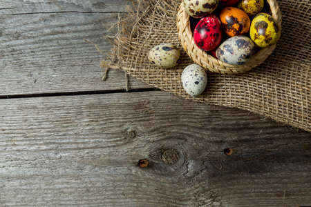 Multi-color dyed Hand painted easter eggs in wicker basket on burlap napkin on wooden background....
