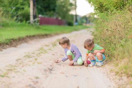 Children draw with a stone on the sand while squatting on a sandy village road.の写真素材