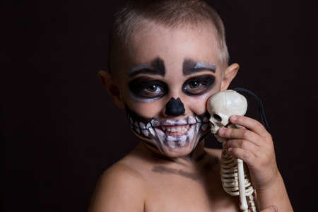 .Close-up portrait of a small child in scary makeup on a halloween on a black background.の写真素材