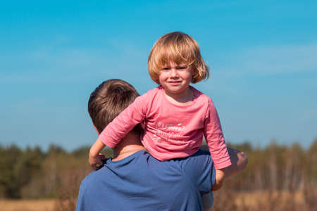 Father's day. Father carries his daughter in his arms in the summer field with dry grass and...