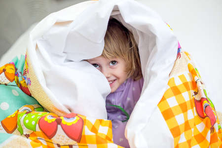 christmas morning, little girl in pajamas hides playing under the blanket in the room with the...