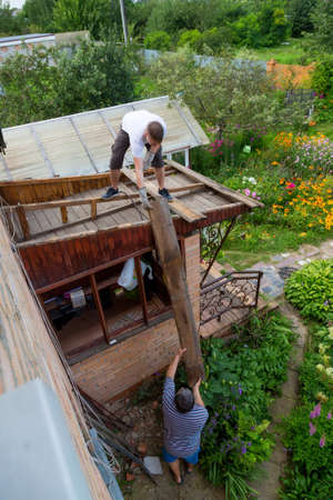 A man is holding an old rotten wooden plank from parsing a roof.の写真素材