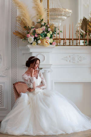 The bride in a white wedding dress sits thoughtfully in a chair waiting for the groom.の写真素材