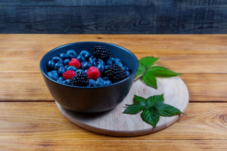 blueberry berry in dark gray ceramic bowl on wooden cutting board on dark blue wooden background.