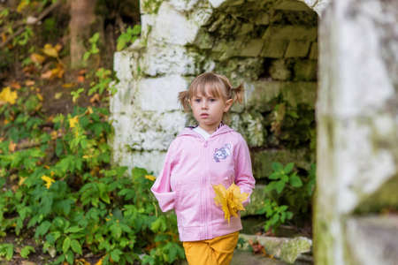 A girl with a broken arm stands near a brick wall in an old park