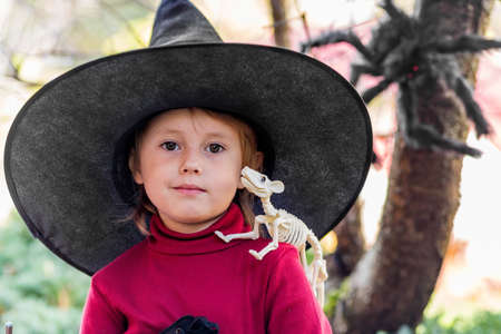Little girl in witch costume making different faces on halloween party in the gardenの写真素材