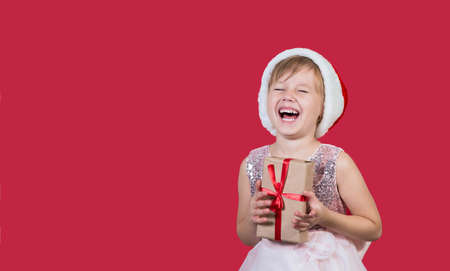 Surprised funny caucasian cute child girl in santa hat looking at the camera, smiling widely happily...