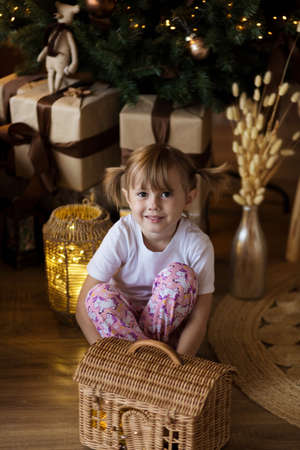 .Girl in pajamas sits on the floor in front of the Christmas tree and plays.の写真素材