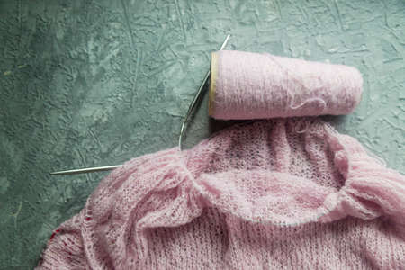 Knitting background flatlay. Bobbin of pink yarn, knitting needles, a knitted pullover on a concrete...