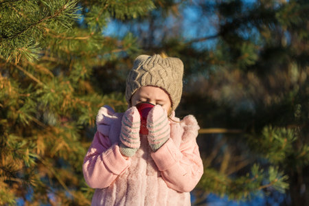 Cute Little girl is drinking from a cup In Winter forest. Happy childhood. Kids Outdoors.Winter Fun Holiday Conceptの写真素材