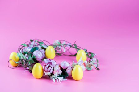 Colored Easter wreath and plastic eggs on a pink background.