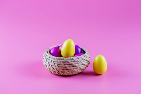Colorful Plastic Easter Eggs in a wicker basket on pink background.