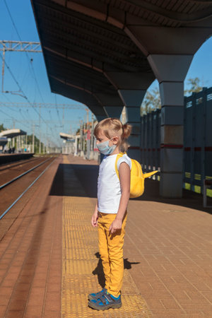 Little girl in a T-shirt and jeans and a medical mask waiting for the trainの写真素材