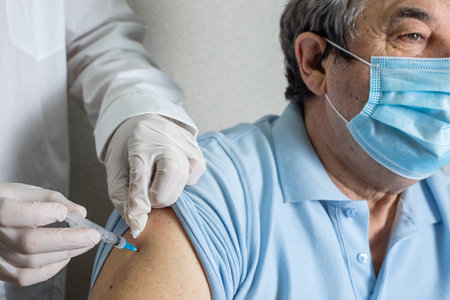 Doctor holding syringe with vaccine. Medical worker vaccinating an elderly patient against flu, influenza, pneumoniaの写真素材