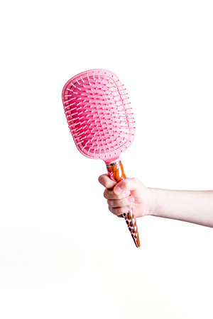 Beautiful pink comb brush in the hand of a girl on a white backgroundの写真素材