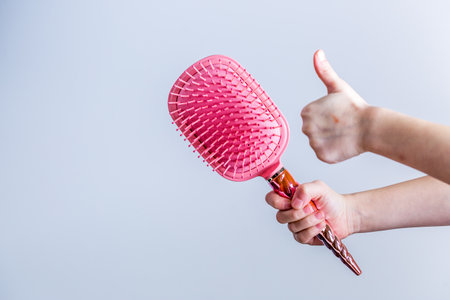 Beautiful pink comb brush in the hand of a girl with thumb up on white background. Women's Hair Care...
