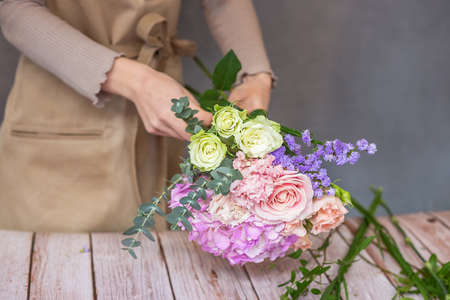 Florist at work. Female hands collect a romantic bouquet of roses. People in the process of work. The concept of a flower shop and flower delivery as a family business.の写真素材