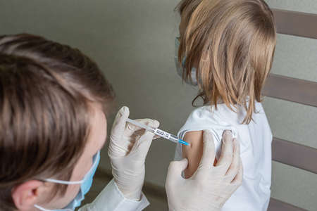 Doctor in a medical mask and gloves makes an injection of a vaccine against a virus infection into...
