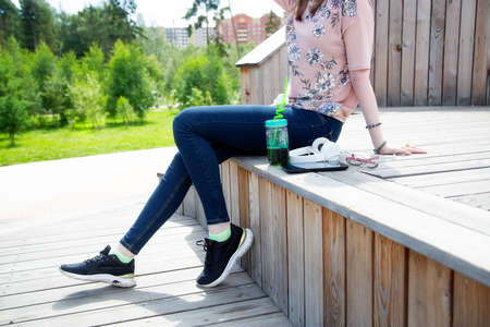 Cropped view of young girl sitting on a wooden podium in the park on a summer day The girl is dressed in a floral T-shirt and jeansの写真素材
