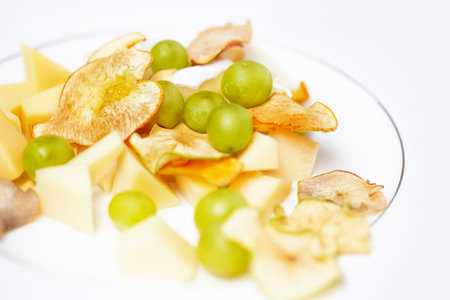 Cheese plate for breakfast with slices of various cheeses, dried apple wedges and grapes.の写真素材