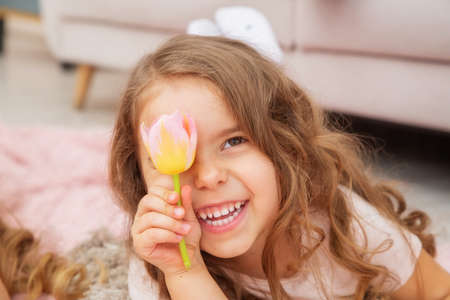 A little girl of Caucasian appearance lies on the floor in a bright living room in a Scandinavian...