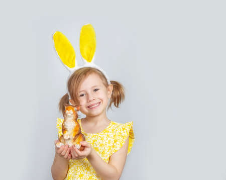 Portrait of a little cute Caucasian smiling girl with bunny ears and decorations for Easter in hands...