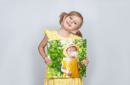 A Little Caucasian girl holding a photobook with her photographs in her hands, advertisement posing against studio wall. Advertising conceptの写真素材