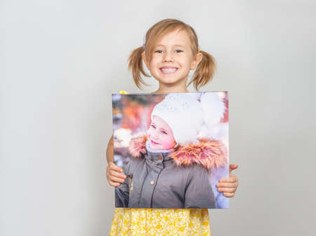 A Little Caucasian girl holding a photobook with her photographs in her hands, advertisement posing against studio wall. Advertising conceptの写真素材