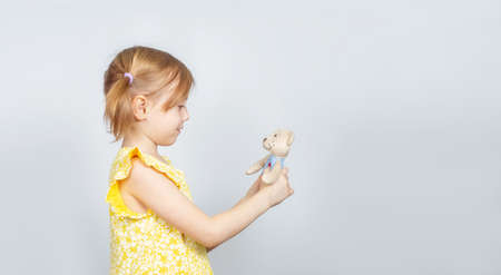 Little Caucasian girl with teddy bear standing sideways to the camera, advertisement posing against studio wall. Advertising conceptの写真素材