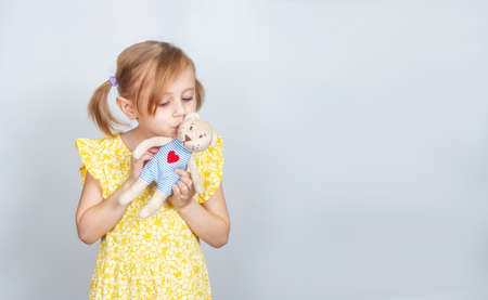 Little Caucasian girl with teddy bear kissing her toy bear, advertisement posing against studio wall. Advertising conceptの写真素材