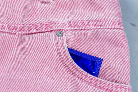 Close-up of a pocket of pink jeans from which a condom sticks out, safe sex conceptの写真素材