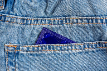 Close-up of a pocket of blue jeans from which a condom sticks out, safe sex conceptの写真素材
