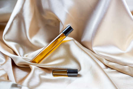 A container for storing cosmetics made of dark glass lie on the folds of a silk satin fabric. Scent fragrance cosmetic beauty product.の写真素材