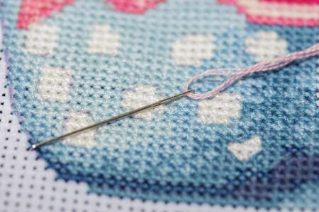 Close-up on a sewing needle with a thread lying on top of a cross-stitched section of a canvas with a pattern. piece of embroideryの写真素材