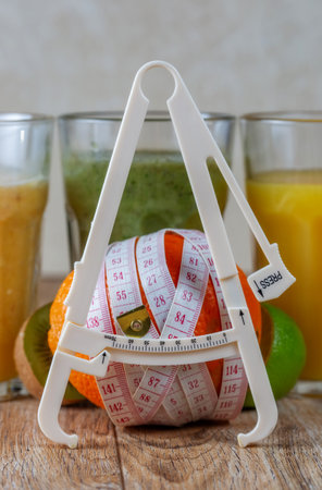 Tall glasses of kiwi and spinach smoothies in a row surrounded by fruits and caliper on a wooden table. The concept of losing weight and proper nutrition.の写真素材