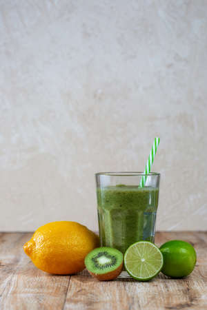 Tall glass with kiwi and spinach smoothie surrounded by fruits on a wooden table. The concept of losing weight and proper nutrition.の写真素材