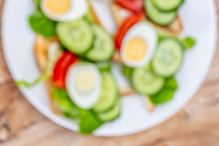 Fried white bread toasts with vegetable and egg slices on a plate, blurred out of focus ediable...