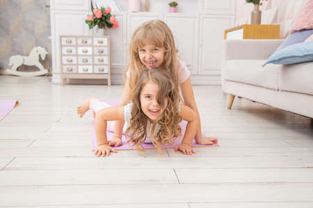 Horizontal photo of couple little girls playing on yoga mat smiling in living room, healthy life habits and lifestyle concept.の写真素材