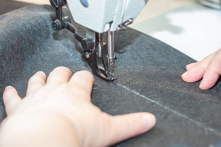 A woman seamstress sews a black cloth on an industrial sewing machine, sewing process