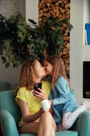 Happy caucasian mom sitting in a chair with her daughter and kissing each other.
