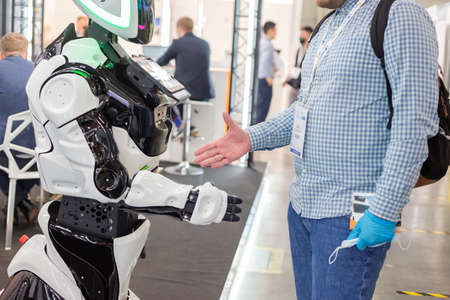 Moscow, Russia - 14 April 2021: An exhibition visitor shakes hands with an intelligent robot at one of the stands at the International exhibition of transport and logistics servicesのeditorial素材