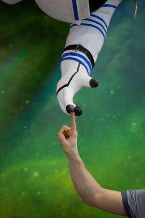 A man hand reaches out to the hand of the model of the astronaut and touches with a fingerの写真素材