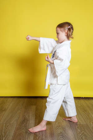 Portrait Of 5 year old caucasian Girl in kimono Practicing Karate Against yellow Background at homeの写真素材