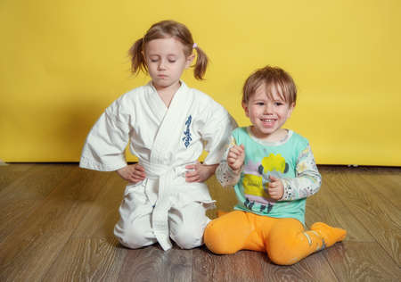 A girl in a white kimono meditates with her eyes closed while her little brother plays and repeats after herの写真素材