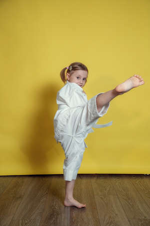 Portrait Of 5 year old caucasian Girl in kimono Practicing Karate Against yellow Background at homeの写真素材