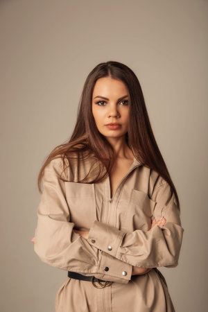 Portrait of young caucasian brunette woman in a beige blouse posing and looking at the camera over beige backgroundの写真素材