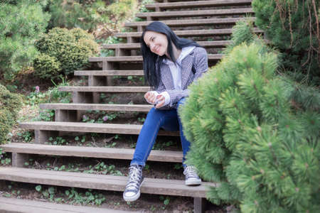Portrait of young brunette woman in a plaid coat in park and looking away enjoying the nature in beautiful spring dayの写真素材