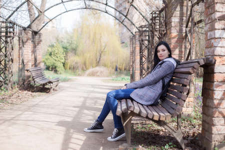 Portrait of young brunette woman in a plaid coat in park and looking away enjoying the nature in beautiful spring dayの写真素材